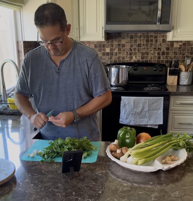 John cutting parsley and garlic on a board with celery, mushrooms, onion and ginger waiting on a platter